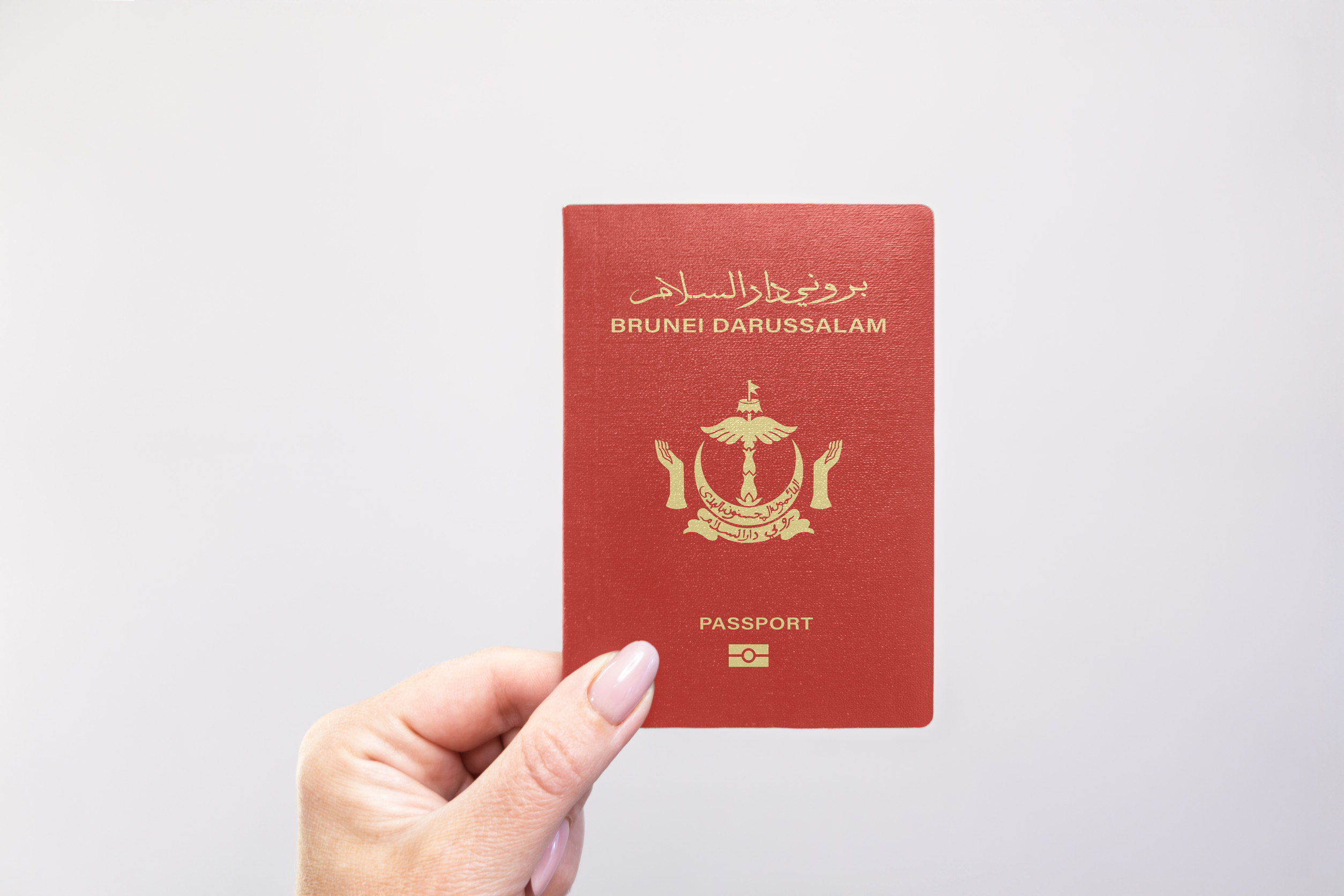 Brunei Passport Held In Hand Against A Plain White Background