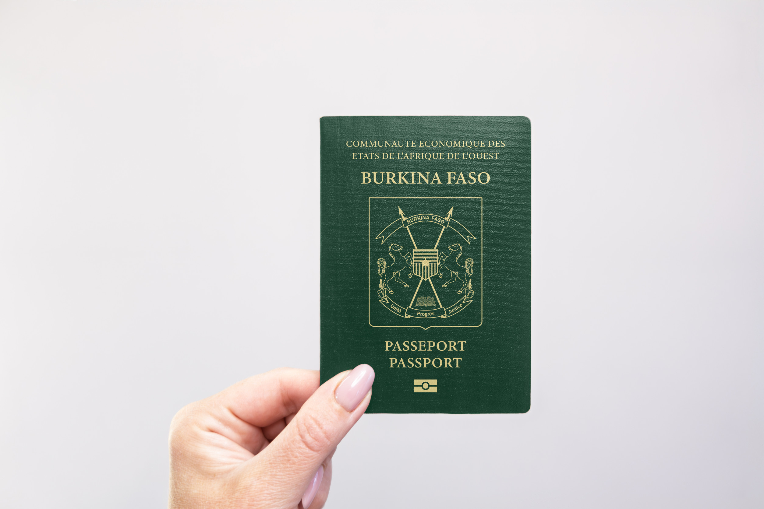 Burkina Faso Passport Held In Hand Against A Plain White Background