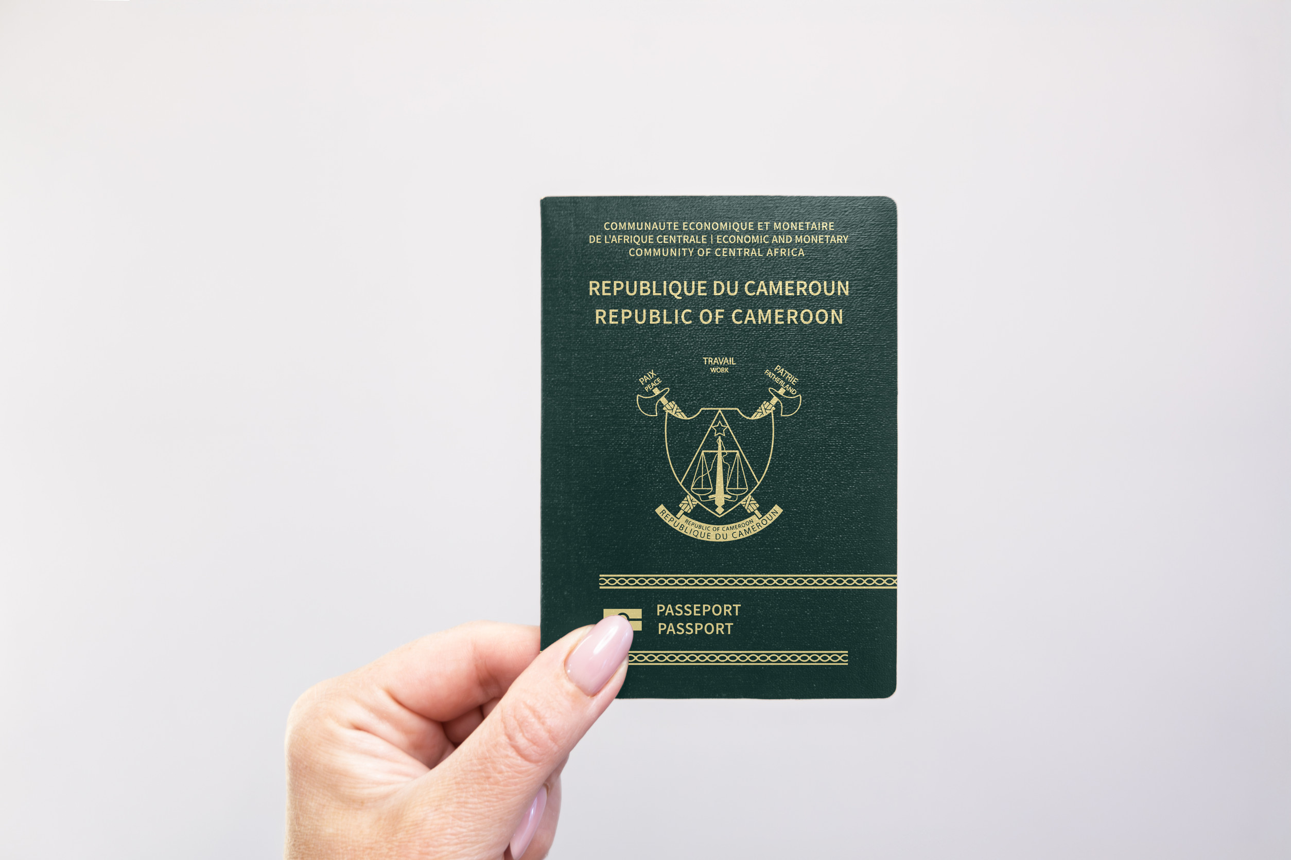 Cameroon Passport Held In Hand Against A Plain White Background